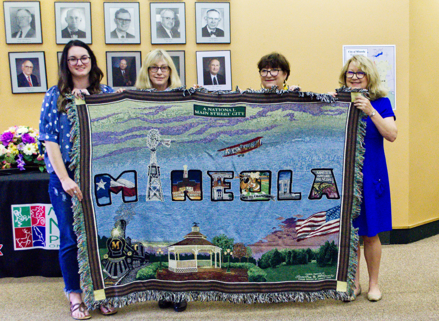 Mural artist Lauren Pitre shows off the new Mineola mural throw rug with museum board members Sharon Chamblee and Wanda Dubbs and Main Street Manager Doris Newman.